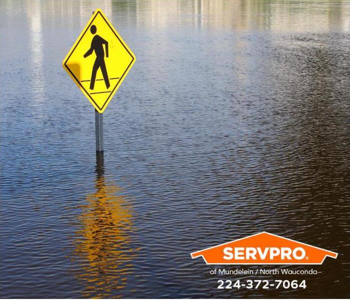 A pedestrian crossing sign and street are submerged by flood waters.